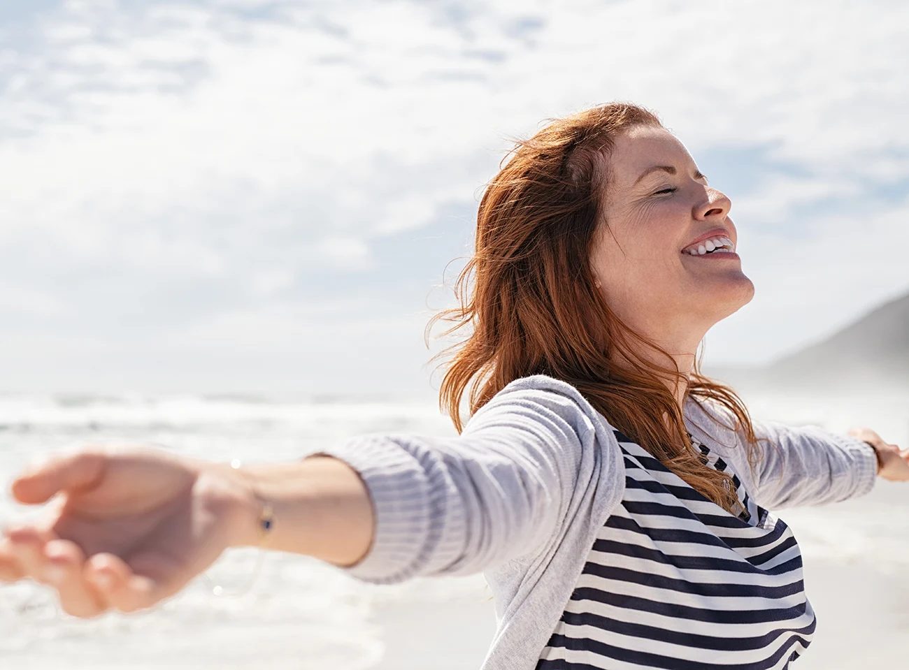 Smiling woman with arms outstretched enjoying ocean breeze at the beach
